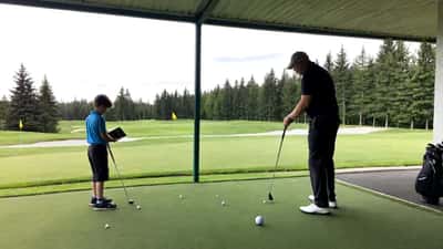 Entraîneur sportif de golf supervisant un élève sur un practice canadien avec tablette d'analyse