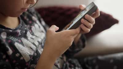 Bambino che gioca con lo smartphone sul divano di casa, simbolo dei minori online su piattaforme come Roblox