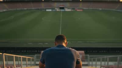 Calciatore professionista seduto sulle tribune di uno stadio vuoto al tramonto, postura pensierosa, simbolo dello stress durante il calciomercato