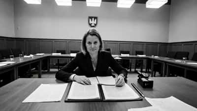 Kvindelig dansk politiker sidder ved et parlamentarisk bord med juridiske dokumenter og det danske flag i baggrunden