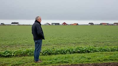 Dansk landmand alene på en mark i Jylland med overskyet himmel — symboliserer rural ensomhed