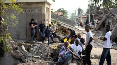 Residentes portugueses avaliando danos em edifício após sismo, com paredes rachadas e detritos