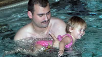 Vater hilft Kind beim Schwimmenlernen – Eltern-Kind-Kurs in österreichischem Hallenbad
