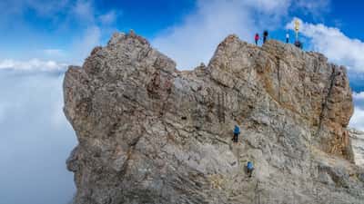 Wanderer auf dem Zugspitze-Gipfel mit Blick auf das Gipfelkreuz bei klarem Herbsthimmel