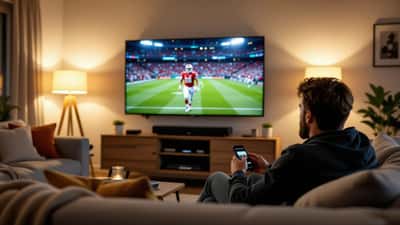 Mand justerer soundbar under et stort tv, der viser en fodboldkamp, i en dansk stue om aftenen
