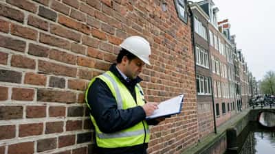 Nederlandse bouwkundige inspecteert diagonale scheur in bakstenen buitenmuur van een grachtenpand in Amsterdam