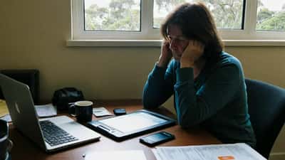 Australian woman looking concerned at a laptop showing a suspicious travel booking confirmation email at home