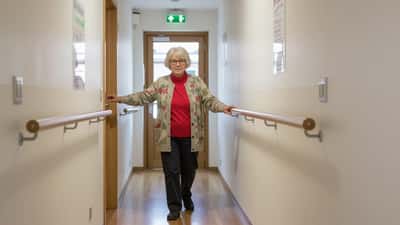 Senior femme âgée marchant prudemment dans un couloir suisse, appui sur la paroi, style photo documentaire