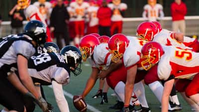 American football players in helmets competing in a game, illustrating contact sport collision risk