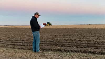 Prairie farmer reviewing financial documents in a spring field at dawn, facing tariff-driven financial pressure in 2026 planting season