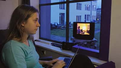 Kvinde ser serie på skærm i lejlighed om aftenen, blå TV-lys i baggrunden