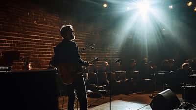 Tónlistarmaður á sviði á tónlistarstað í Reykjavík með tóma stóla og veggljós