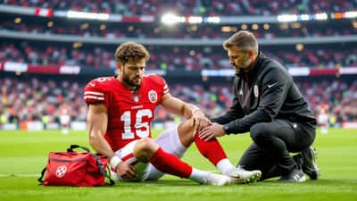 Junger Fußballprofi mit Beinverletzung am Spielfeldrand, Physiotherapeut leistet Erste Hilfe