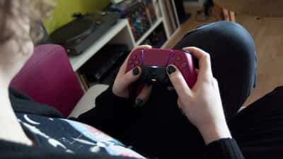 Person hält einen weißen PlayStation 5 Controller, Nahaufnahme Gaming Jugendschutz