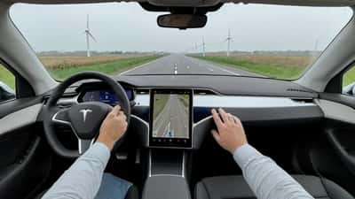 Tesla bestuurder met handen boven het stuur op een Nederlandse snelweg met FSD-navigatie actief op het scherm