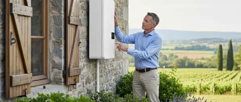 Propriétaire examinant une pompe à chaleur blanche installée sur le mur extérieur d'une maison en pierre dans la campagne française