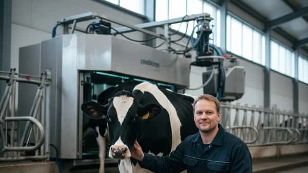 Suomalainen viljelijä tarkastaa Holstein-lehmää modernissa navettarakennuksessa lähellä Pirkkalaa, lypsyrobotti taustalla