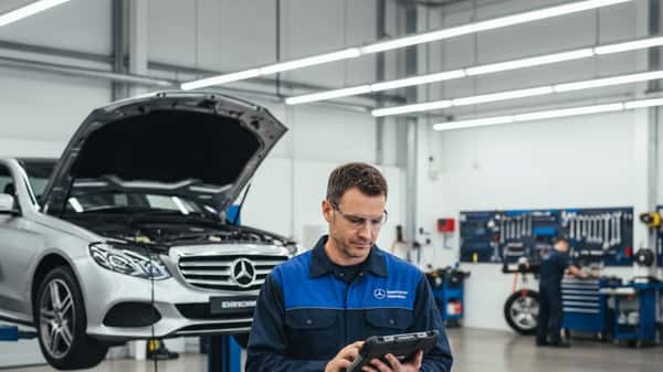 Australian mechanic using diagnostic tablet next to a Mercedes-Benz E-Class on a hydraulic lift in a Sydney automotive workshop