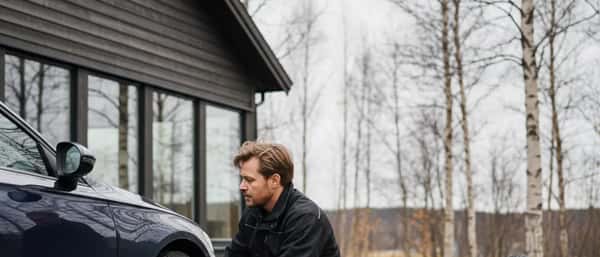 Nordmann skifter dekk på sin bil i innkjørselen en grå høstdag, med stabel vinterdekk i bakgrunnen