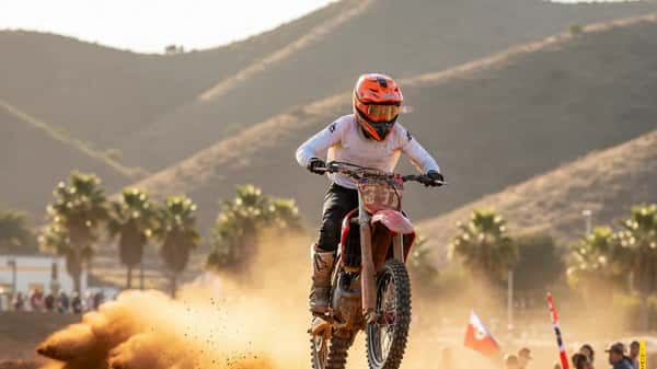Piloto latino de motocross saltando en un circuito de tierra en California con polvareda y sol de tarde