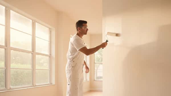 Pintor hispano profesional aplicando pintura con rodillo en una sala de estar de Miami con luz natural