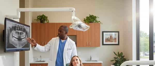 Dentist in blue scrubs explaining an X-ray to a patient in a modern dental office with natural light