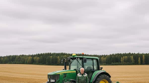 Suomalainen viljelijä seisoo John Deere -traktorin vieressä syksyisellä pohjalaisella pellolla harmaana pilvisenä päivänä