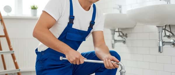 Nederlandse loodgieter in blauwe overall repareert een koperen leiding onder een keukenaanrecht