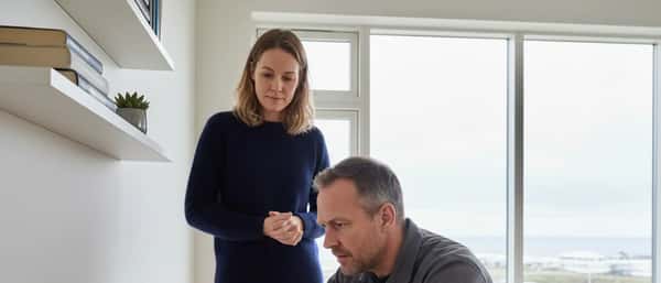 Tölvutæknifræðingur skoðar fartölvu í íbúð í Reykjavík meðan viðskiptavinur horfir á