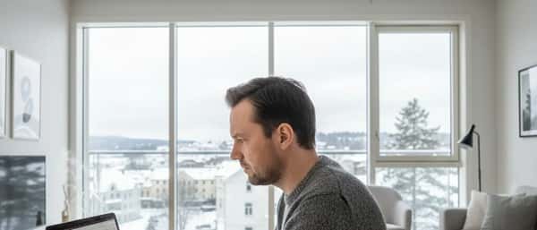 Mann i grå genser gjennomgår investeringsdata på laptop i en moderne norsk leilighet med dagslys