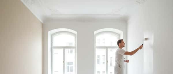 Professioneller Maler streicht eine Altbauwand in einer Berliner Wohnung mit weißer Dispersionsfarbe