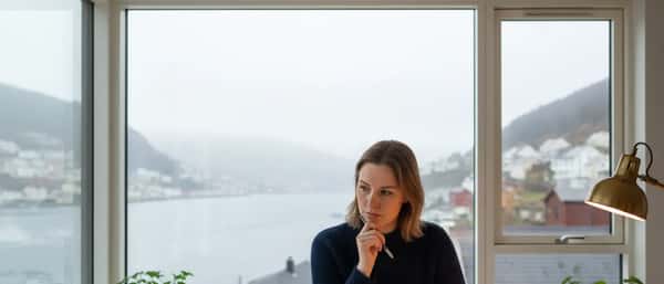 Norsk kvinne studerer boliglånsdokumenter ved kjøkkenbord i Bergen-leilighet med fjord-grått dagslys