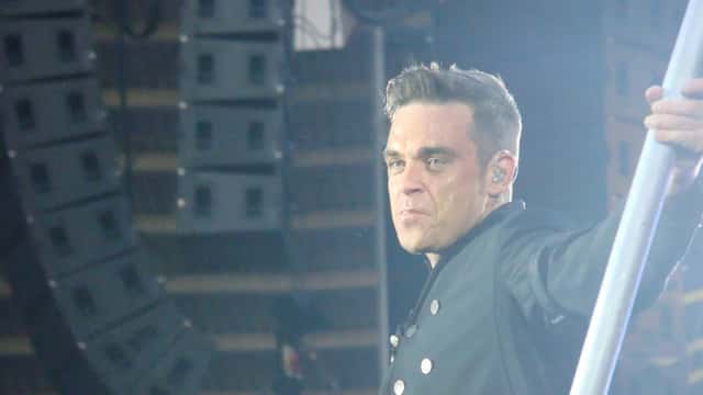 Robbie Williams optræder live ved udendørskoncert, syngende på scenen foran et stort publikum