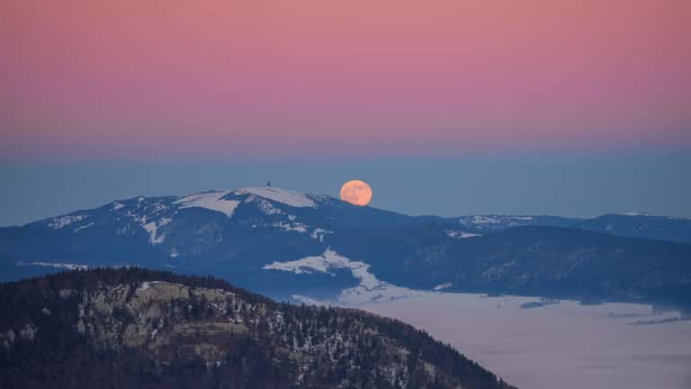 A large amber full moon rising at sunset behind the Swiss Alps, Chasseral