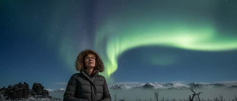 Frau mit Brille schaut nachts auf Polarlichter am deutschen Himmel