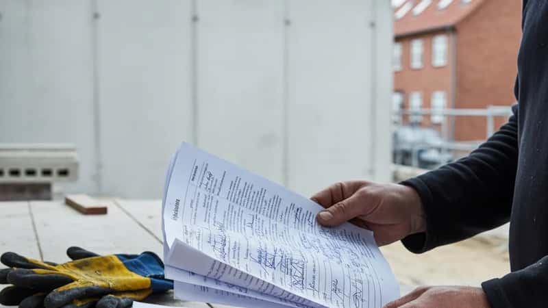 Tømrer sammenligner lønoverenskomst dokumenter på en byggeplads i Aarhus — hands-on gennemgang af Bygningsoverenskomsten 2025-2028