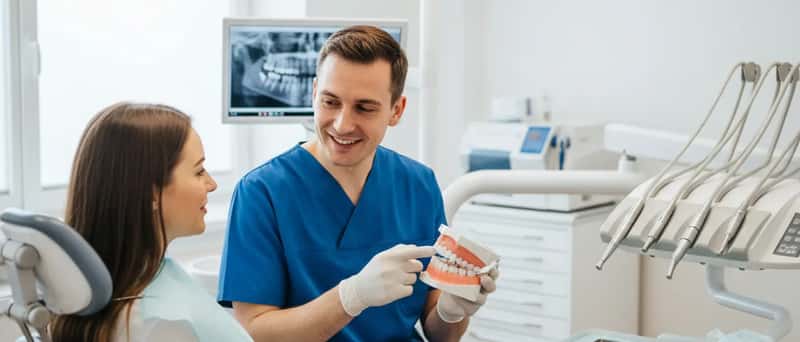 Dentist explaining treatment options to a patient using a dental model in a bright UK dental surgery