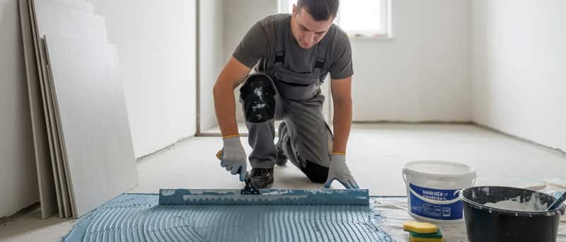 Artisan appliquant une membrane d'étanchéité sur un sol de salle de bain avant la pose de carrelage