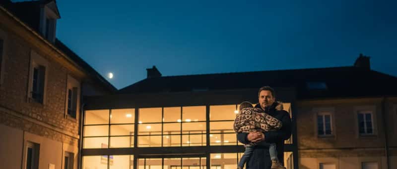 Entrée des urgences d'un hôpital cantonal suisse la nuit, un homme portant un enfant s'approchant des portes éclairées