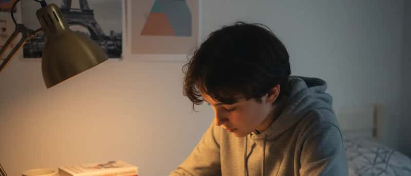 Adolescent français révisant du vocabulaire anglais dans un cahier, à son bureau sous une lampe chaleureuse