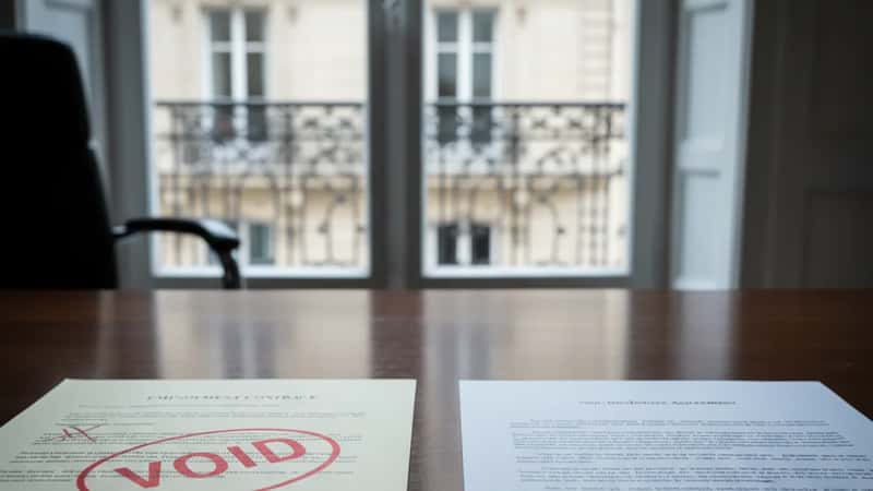 Two employment contracts on a Montana law office desk - one stamped VOID in red and one NDA agreement, cool natural window light, legal comparison