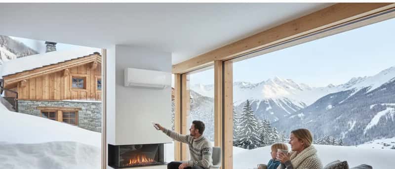 Norsk familie i stue med varmepumpe på veggen, far justerer fjernkontroll mens mor og barn sitter i sofaen