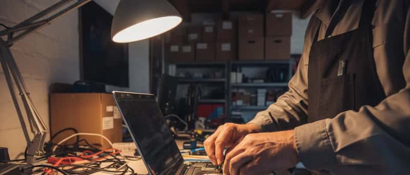 Nærbilde av hender som bytter harddisk i en laptop på et verksted