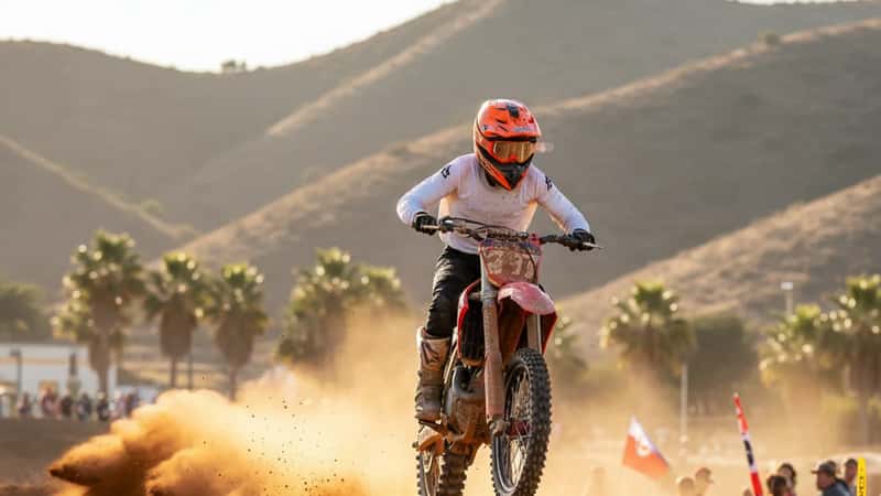 Piloto latino de motocross saltando en un circuito de tierra en California con polvareda y sol de tarde