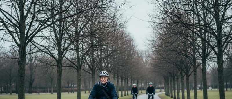 Dansk mand cykler på en sti gennem en bypark med bare træer og overskyet himmel