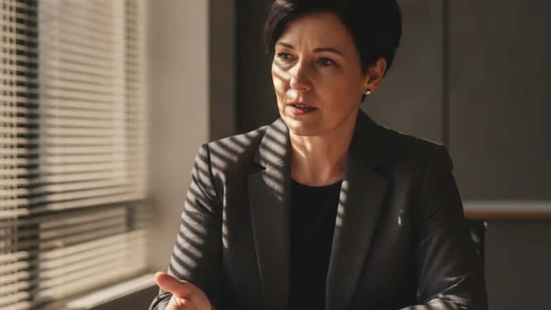 An Australian financial adviser in an Adelaide CBD office gestures to a printed superannuation contribution breakdown across a meeting table, warm venetian blind light, professional setting