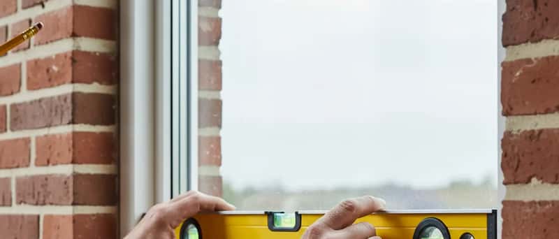 Tømrer monterer et nyt vindue i et dansk parcelhus med vaterpas og præcisionsværktøj