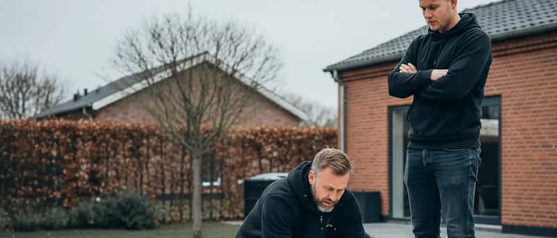 To tømrere gennemgår byggeplaner på en halvfærdig terrasse i en dansk parcelhushave