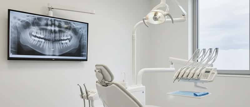 Behandlungsraum einer deutschen Zahnarztpraxis mit Behandlungsstuhl, Instrumententray und Röntgenbild am Bildschirm
