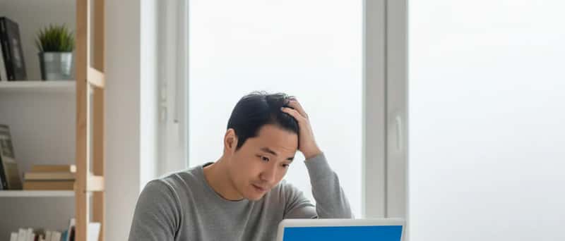 Frustrated man looking at a laptop with a blue error screen on a home office desk